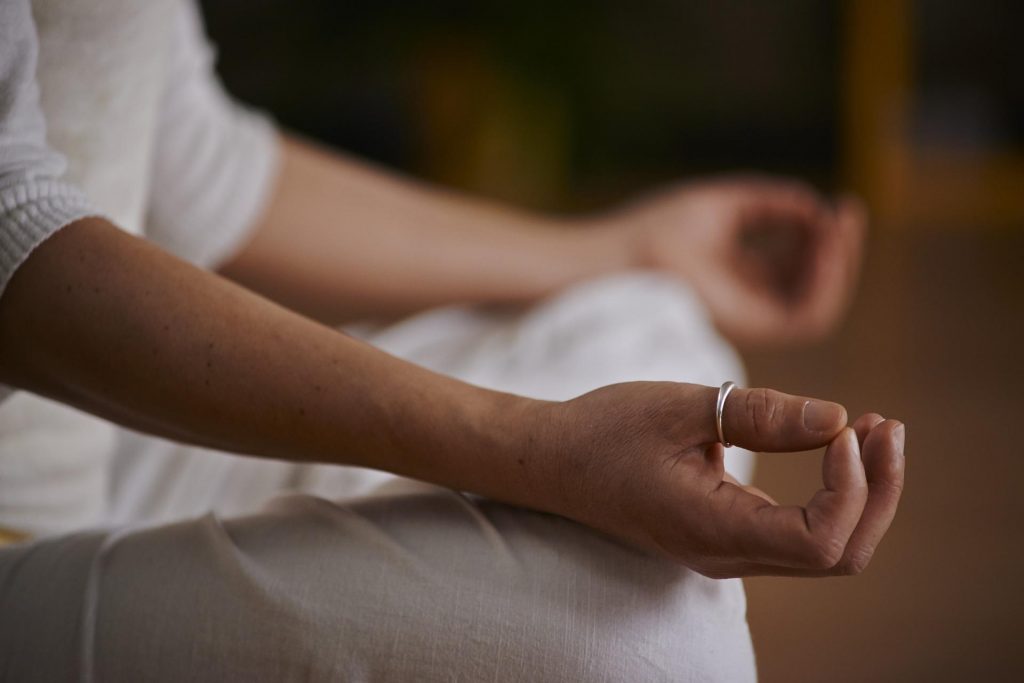 Image of a person meditating with fingers touching. Yoga and meditation can improve the HRV of people with Long Covid.